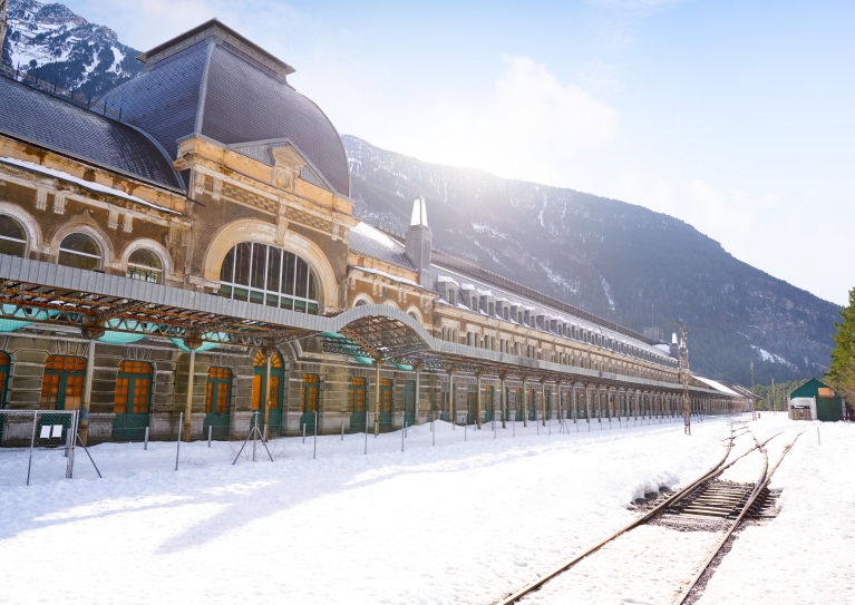 An ornate train station in the snow, with mountains in the background