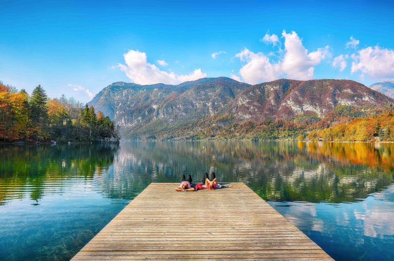 Vista de un muelle en el lago Bohinj, con árboles otoñales al fondo