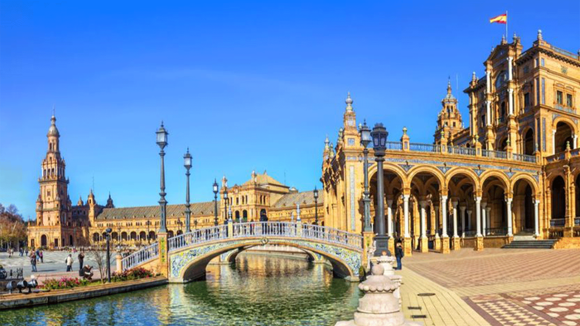 An old, stately building with a colonade next to a bridge over a body of water in a plaza