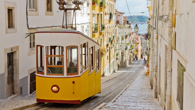 A yellow tram running up a street in Lisbon