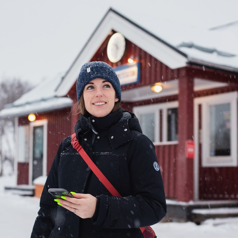 A woman in a winter hat and coat stands outside of a snow-covered train station