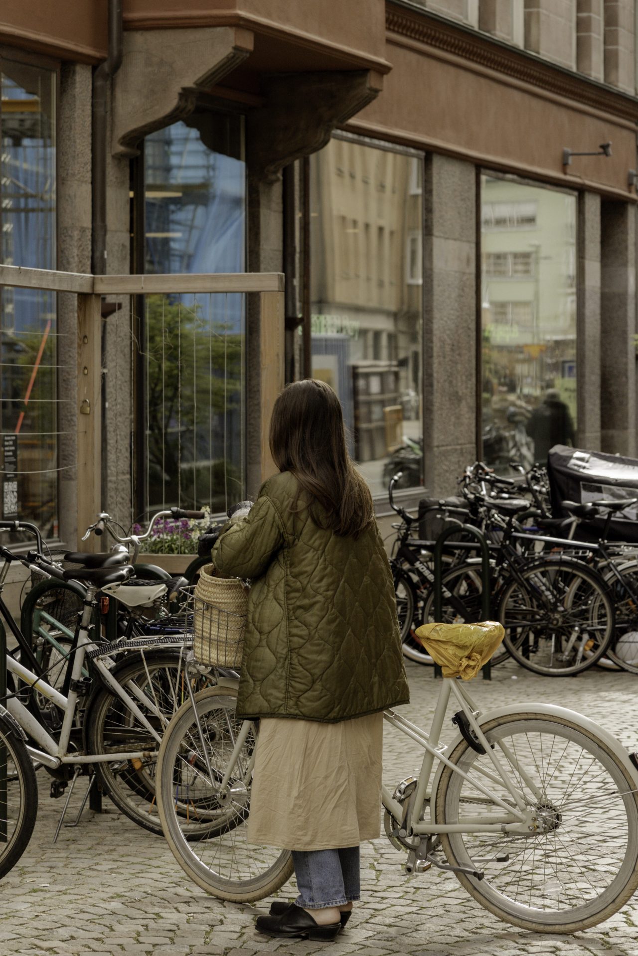 A woman with her back to the camera, holding a bike on a street in Malmo, Sweden